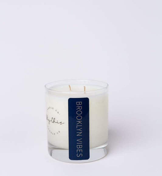 A white candle with a label that reads 'Brooklyn Vibes', set in a clear glass vessel.