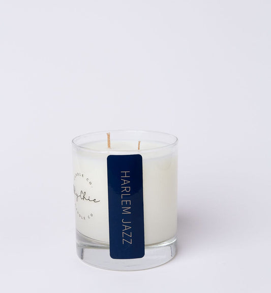 A white candle with a dark label that reads 'HARLEM JAZZ', set inside a clear glass vessel.